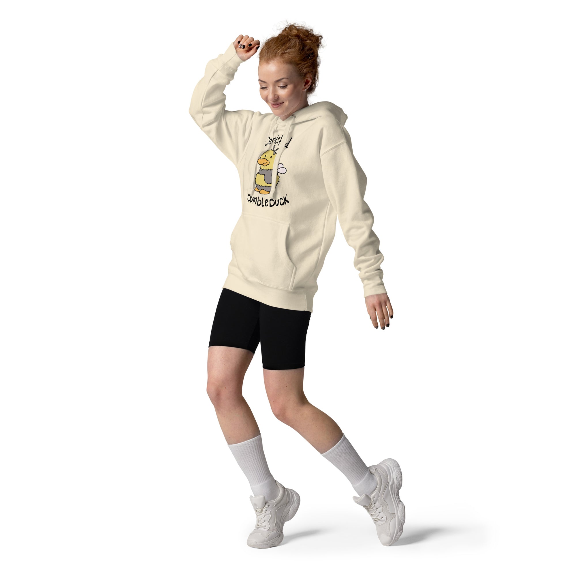 A woman wearing a beige hoodie with a duck character and text CERTIFIED BUMBLEDUCK, black shorts, white socks, and white sneakers on a white background.