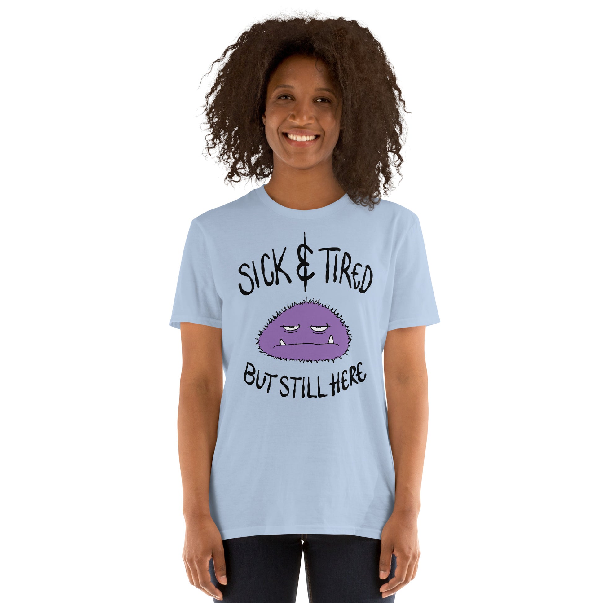 Person wearing a Light blue t-shirt with a purple cartoon character and text sick and tired but still here on a white background