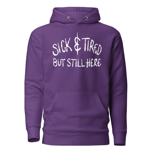 Purple hoodie with white text 'SICK & TIRED BUT STILL HERE' on a white background