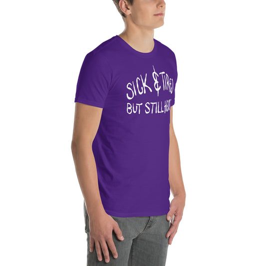 Person wearing a purple t-shirt with text 'SICK & TIRED BUT STILL HERE' on a white background